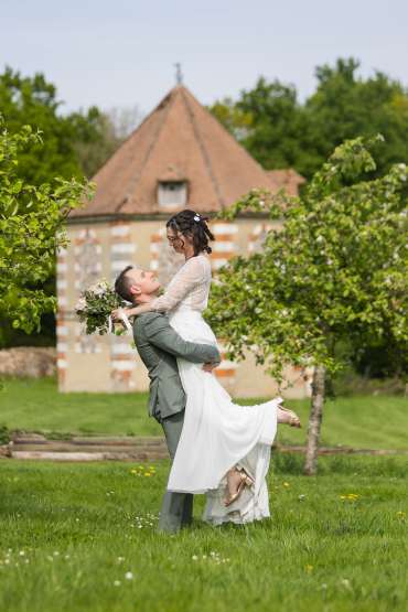 Le marié porte la mariée dans les bras et ils se regardent avec une partie du domaine en arrière plan