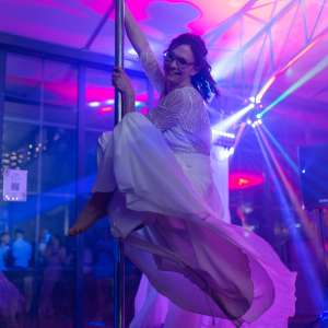 Mariée faisant de la pôle dance en robe de photo d'une mariée avec les couleurs rose et bleues des lumières de la salle de mariage dans un domaine à proximité de Maisons-Laffitte.